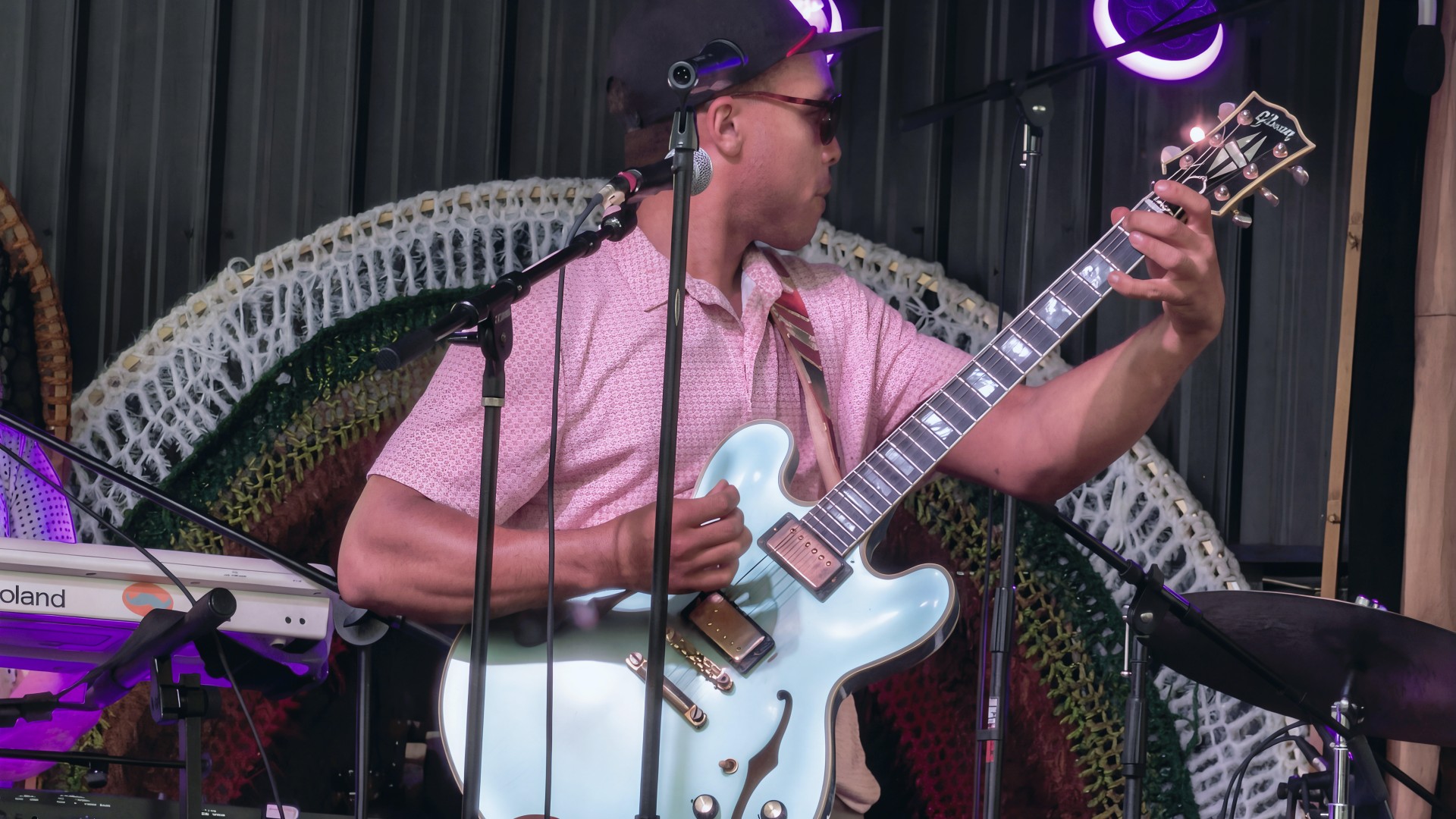 Charlie Berry playing a Gibson hollow-body guitar in a pink shirt and cap